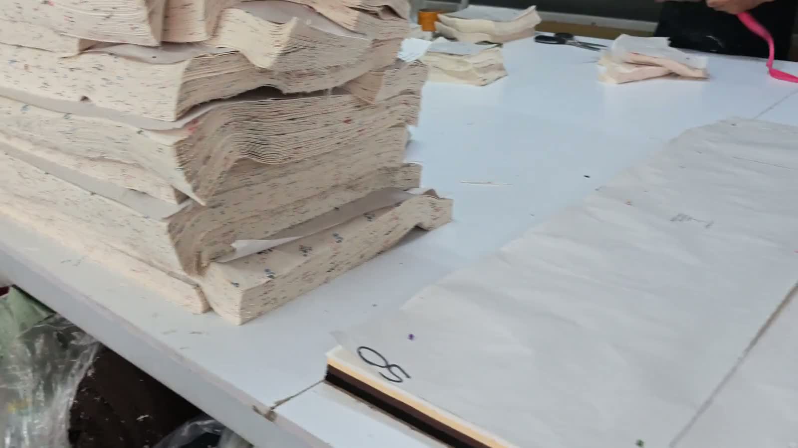 Stacks of cut fabric beside garment patterns on a cutting table